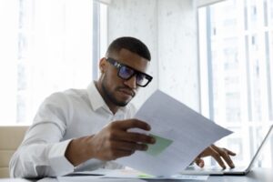 Man reading paper while typing on a laptop